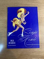 Front cover of 1953 Sonja Henie Ice Revue souvenir program showing illustrated female ice skater in gold costume on blue background.