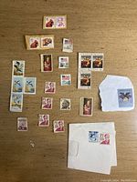 Overall view of various US postage stamps arranged on a wooden surface, including multiple 15 cent Oliver Wendell Holmes stamps, bird-themed stamps, Christmas stamps, and others.