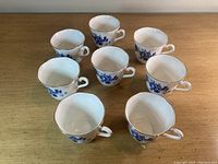 Eight white bone china tea cups with blue rose pattern arranged on wooden table