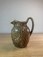 Tan/brown Kingwood ceramic pitcher with grapevine relief pattern, arched handle and curved spout