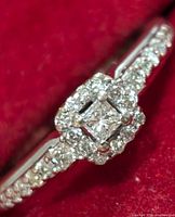 Close-up top-down view of ring showing princess-cut center diamond, halo, and shank diamonds.