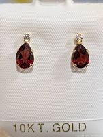 Front view of pair of gold earrings with red and clear stones on white jewelry holder stamped 10KT GOLD.