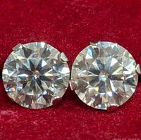 Close-up of two round brilliant-cut moissanite gemstones in four-prong settings on red background