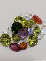 Mixed assortment of polished oval, round faceted gemstones in green, purple, orange, red and clear colors, totaling approximately 10 carats.