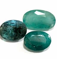 Three oval-shaped emerald gemstones displayed on a white surface, showing clear detail of color and inclusions.