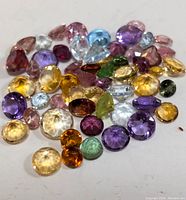 Close-up image of a mixed assortment of faceted multi-colored gemstones, showing variation in cut, size, and color.