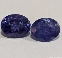 Close-up photo of two oval faceted tanzanite gemstones showing their deep blue and violet colors with visible inclusions.