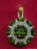 Front close-up of the round pendant showing marquise-cut green chrome diopside stones and clear gemstone accents on red fabric background.