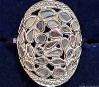 Close-up showing the oval shape, pear-shaped diamonds clustered within and small round diamonds outlining the edge on silver metal base.