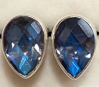 Close-up front view showing the pair of pear-shaped faceted blue gemstone earrings in silver bezel settings.