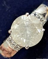 Close-up front view of a silver ring with a large round moissanite center stone and small accent stones on the band.