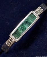 Close-up side angle of silver ring showing rectangular setting and green stones.