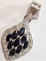 Front view of silver pendant showcasing marquise-cut dark blue sapphires set within a silver frame with small clear stones accent.