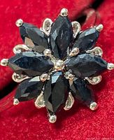 Close-up photo showing a silver ring with eight marquise-cut dark blue sapphire stones arranged in a floral cluster pattern.