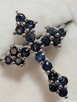 Close-up image of silver ring displaying blue sapphire stones set in cross shape