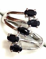 Close-up view of the silver ring's front showing five dark blue oval sapphires in a prong setting arranged on a split band structure.