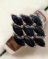 Close-up of the silver ring featuring nine marquise-cut dark blue sapphires set in prongs in a clustered rectangular shape on a polished silver band.