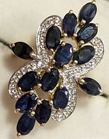 Close-up front angle of silver ring featuring blue marquise sapphires surrounded by small diamonds forming a floral pattern