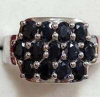 Close-up photo of silver ring with three rows of oval dark blue sapphire stones in cluster setting on a wide shoulder band.