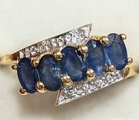 Close-up view of silver ring with five blue sapphire stones held by gold prongs and diamond accents on band.