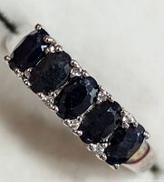 Close-up top view of a silver ring with five rectangular dark blue sapphire stones set side by side, accented by small round clear stones between each sapphire.