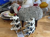 Photo showing two stacks of cast iron animal figurines painted white with black spots along with wire sheep figurine in the background.
