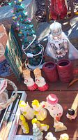 Overall lot showing ceramic Christmas tree, king figure, assorted figure candles, and red candle holders on outdoor surface.