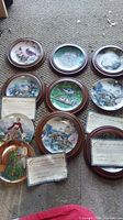 10 collector plates laid out on carpet, including cardinals, blue jays, chickadees and women in period dress, some with Certificates of Authenticity