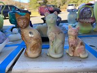Three cat figurines on display outside showing detailed painted and etched floral designs.