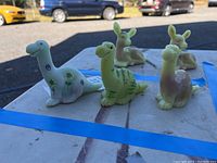 Group shot of three dinosaur figurines on tabletop showing white, green, and pink/lavender pieces