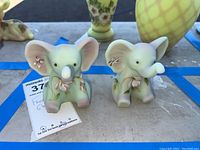 Front view of two small pastel elephant figurines with floral details placed side by side showing their faces and ears.