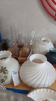 Photo of multiple glass hurricane shades and one white opaque swirled glass lamp shade with a white glass chimney in background
