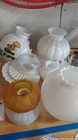 Photo showing group of 9 glass lamp shades including white, amber, and decorated with mushroom designs