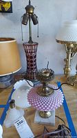 Top view showing ruby red glass lamp, pink hobnail lamp, lamp with beige shade, brass and milk glass lamp, and white ceramic piece.