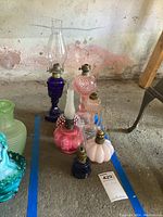 Full view of the seven oil lamps with different glass bases and chimneys arranged on the floor