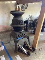 Full view of cast iron pot belly stove and two Stanley hand planes on concrete floor near wooden support structures and electric fans.