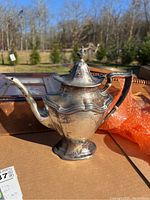 Front left oblique view of teapot on cardboard surface outdoors showing body, spout, lid and handle