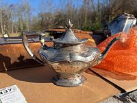 Front left quarter view of tarnished sterling silver teapot showing ornate body, foot, spout, wooden handle and monogram.