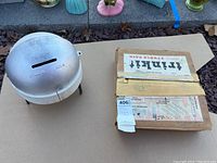 Aluminum studio kiln next to cardboard box labeled 'Trinkit Studio Pack' containing accessories