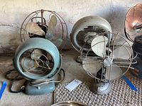 Four vintage electric fans shown together on garage floor, various sizes and brands including GE, Vornado, Arctic Aire, Bond Cain