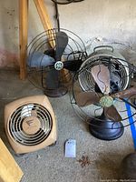 Four vintage fans grouped on floor in a garage-like space, showing front and side views of metal blade fans and the heaterette unit.