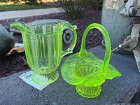 Two yellow uranium glass pieces: creamer and basket sitting outdoors on stone surface, showing vibrant yellow-green color.
