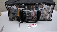 Lot of 35 DVDs stored inside black carrying bag with clear plastic window and two black straps, displayed on white table.