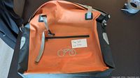 Photo showing the whole orange saddle bag with a bicycle logo on front and a small zipper pocket.