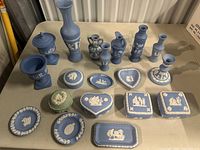 Overview of 17 pieces of blue jasperware ceramics with white classical reliefs displayed on a table.
