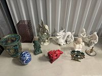 Overview of all ceramic and porcelain decorative items on display including vases, figurines, and small sculptures arranged on a table.