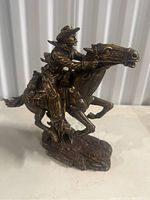 Side view of cowboy riding horse figurine showing detailed saddle and reins.