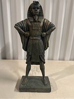 Front and side view of bronze-colored Egyptian pharaoh statue with hands on hips standing on rectangular base.