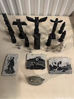 Full lot overview showing eleven black totems, six metal mini totems, one white dog sculpture, and three stone plaques.