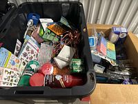 Top-down view of the black bin showing a mix of office supplies such as glue containers, stickers, string lights, and packets of clips.